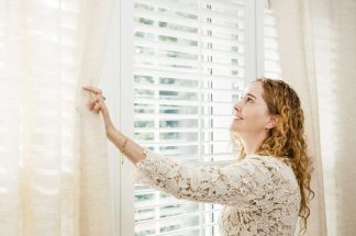 mujer sonriendo abriendo las cortinas de su hogar